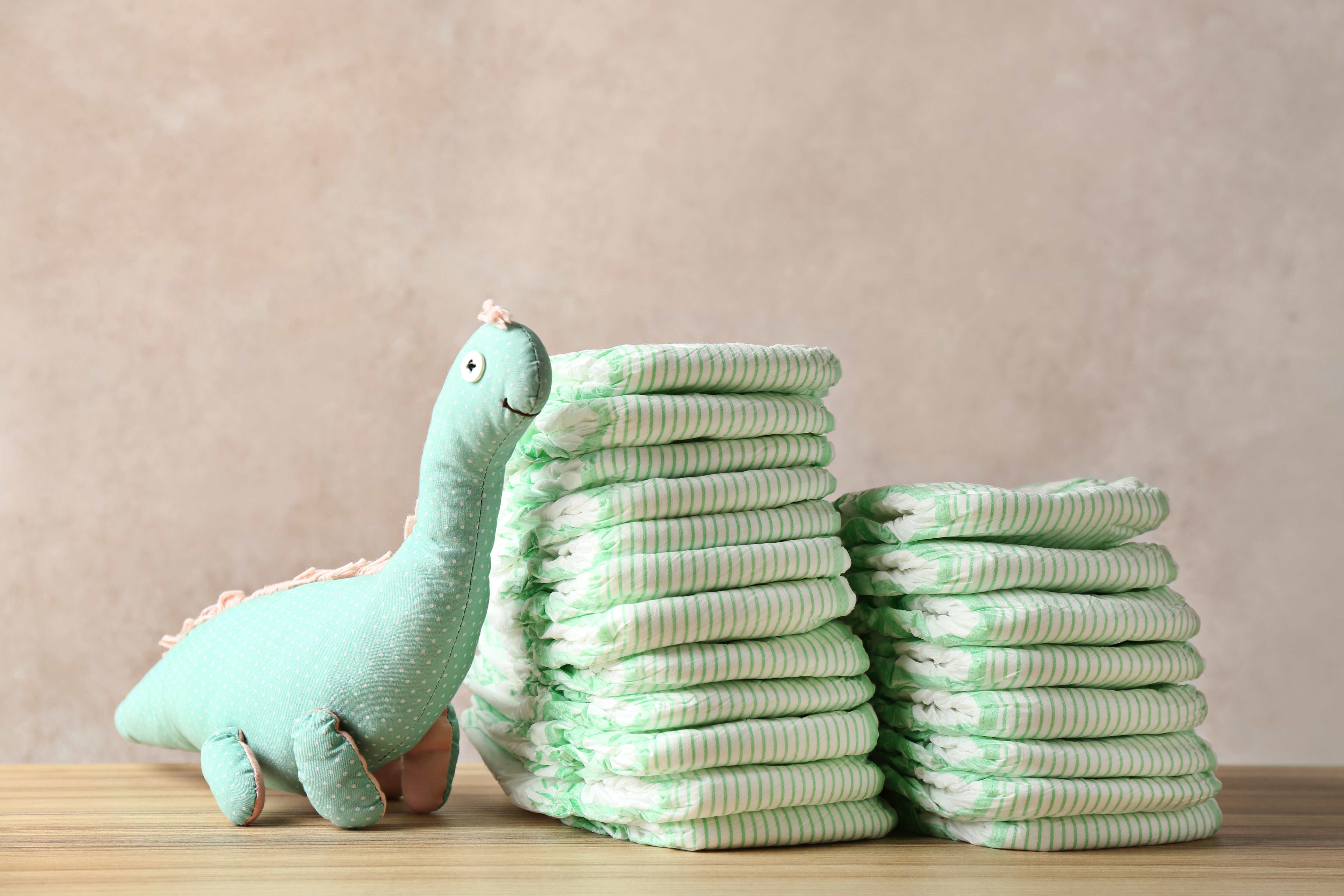 Stacks of baby diapers beside a stuffed dinosaur toy