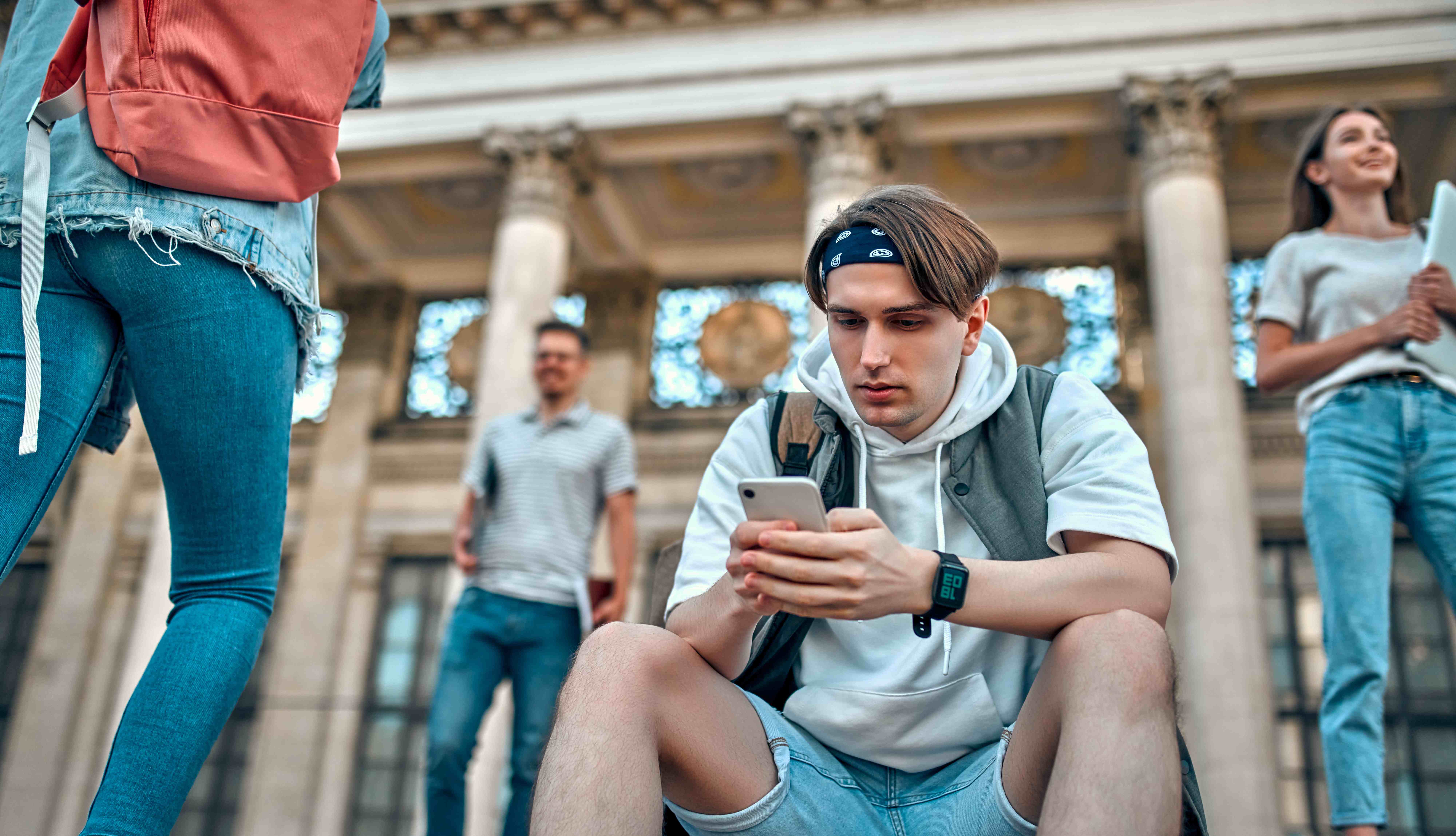 Student looking at his phone on campus steps with friends nearby