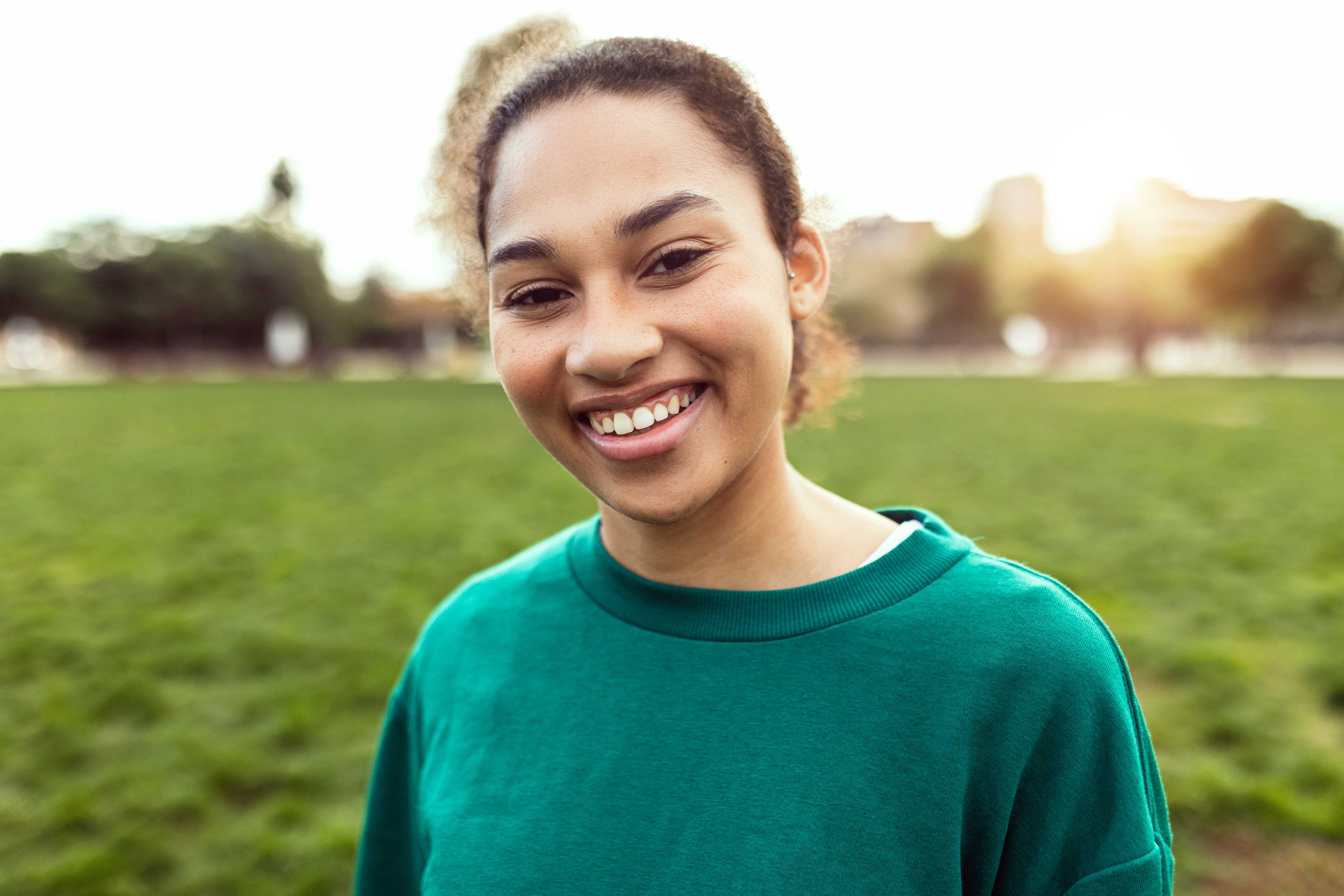 Smiling young woman in a green sweatshirt standing outdoors in a park