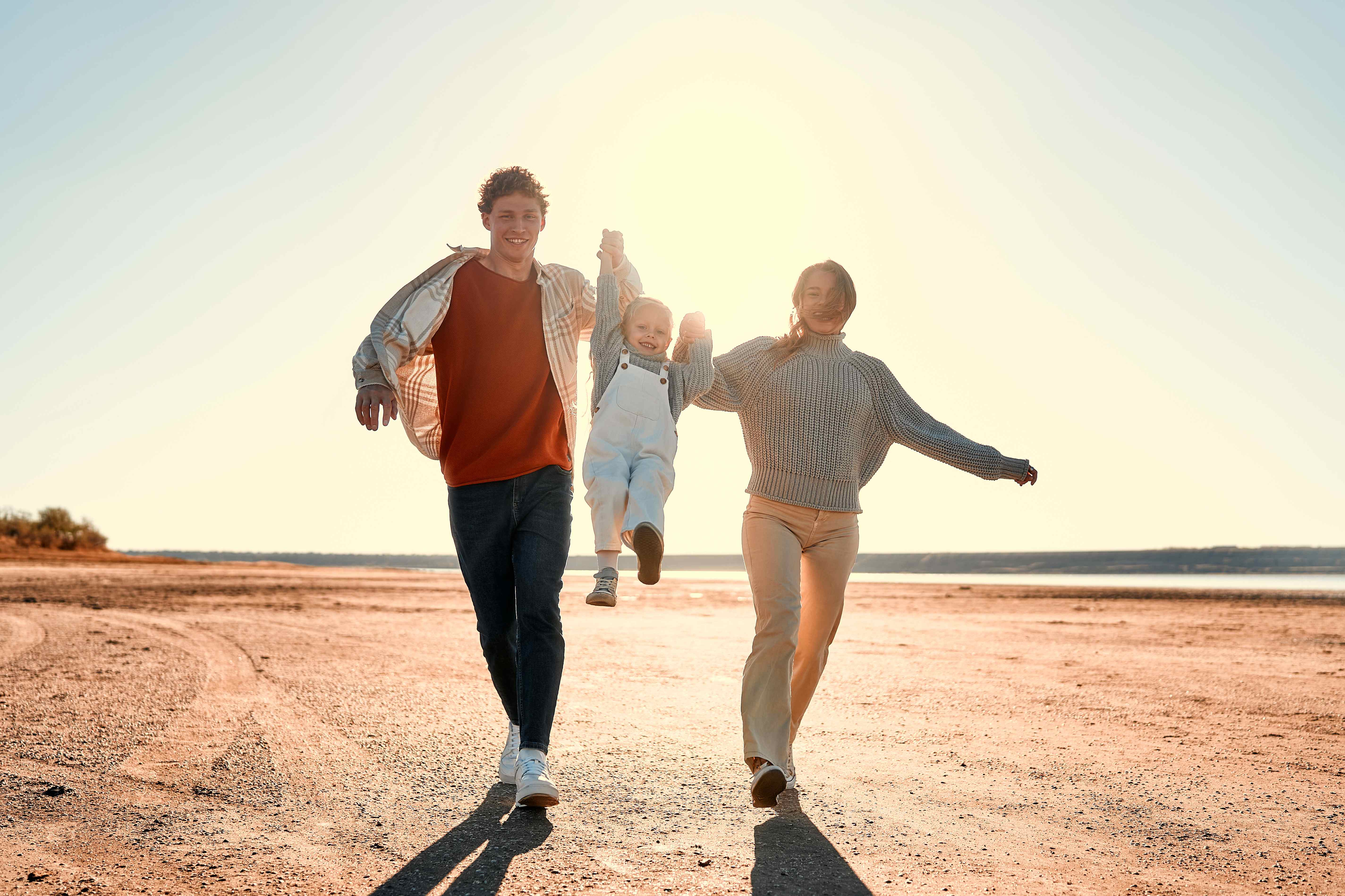 Joyful family running together on the beach at sunset